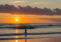 Anfänger-Surfer fängt eine kleine Welle bei Sonnenuntergang.